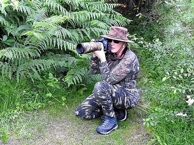 A woman in full camouflage gear crouching down with a camera